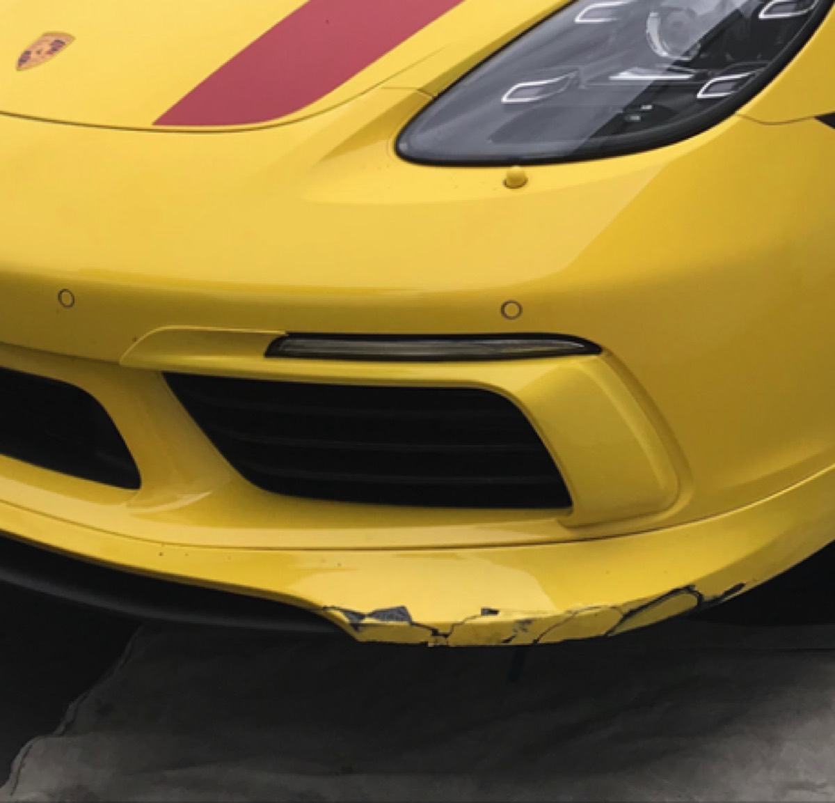 Bumper Crack Repair before in Brea, CA, Cracked and chipped front bumper lip on a Porsche 718, rebuilt, refinished, and color-matched on-site in Orange County.