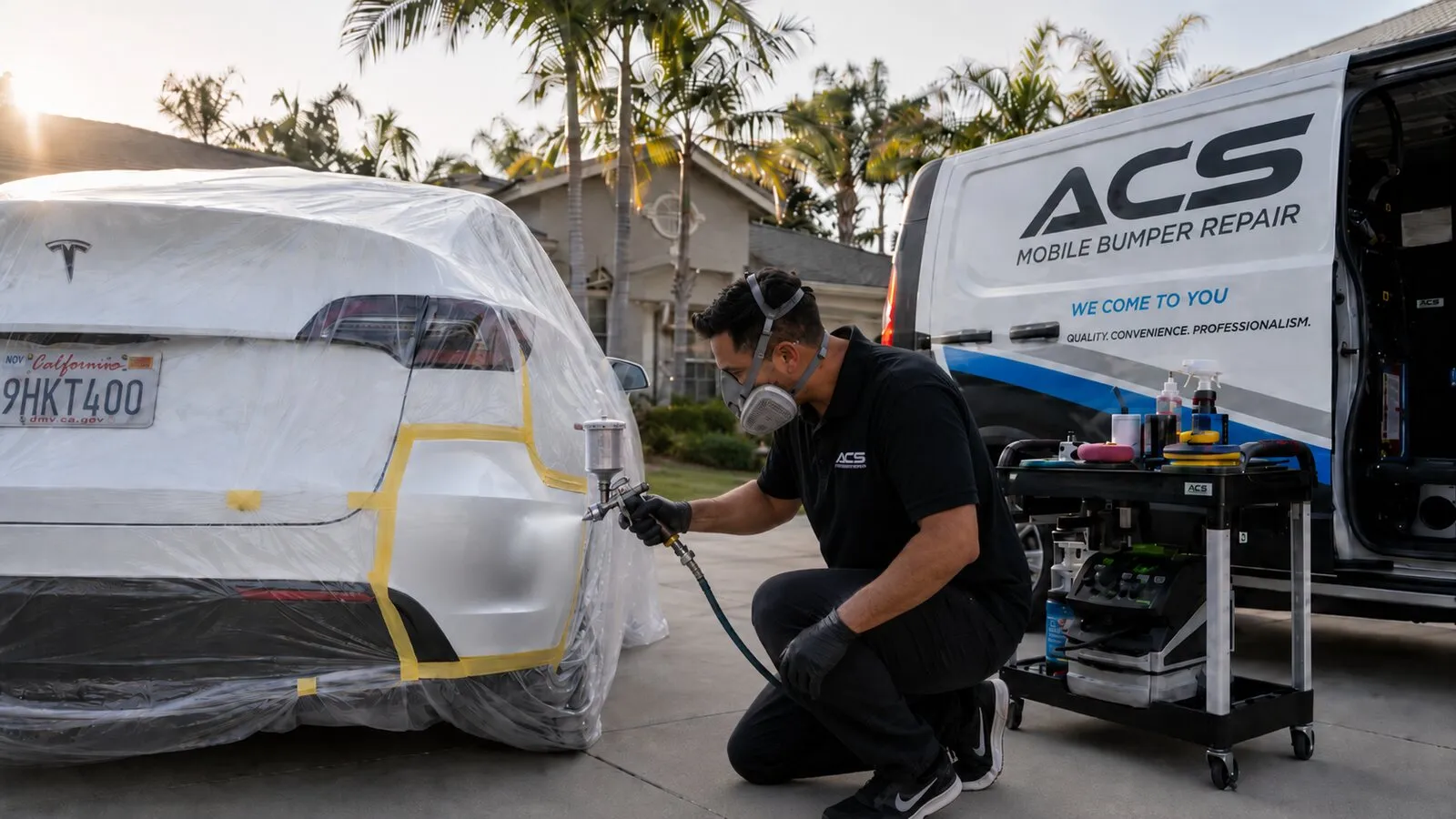 ACS technician spray-painting a masked-off white Tesla rear bumper with an exact PPG color match in Newport Beach, Orange County, the ACS mobile van in the driveway